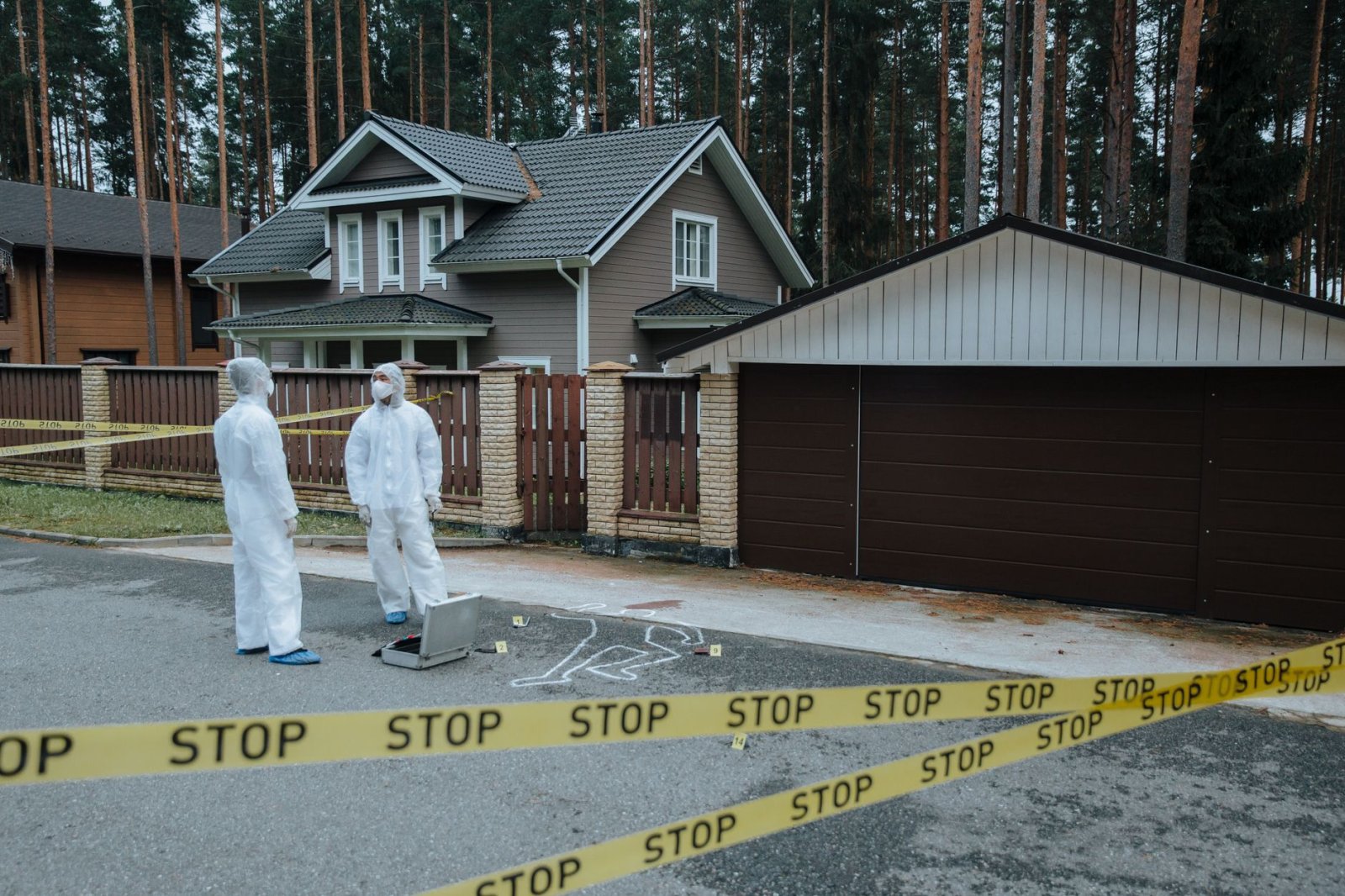 Crime scene investigators in protective suits examining suburban house with yellow tape